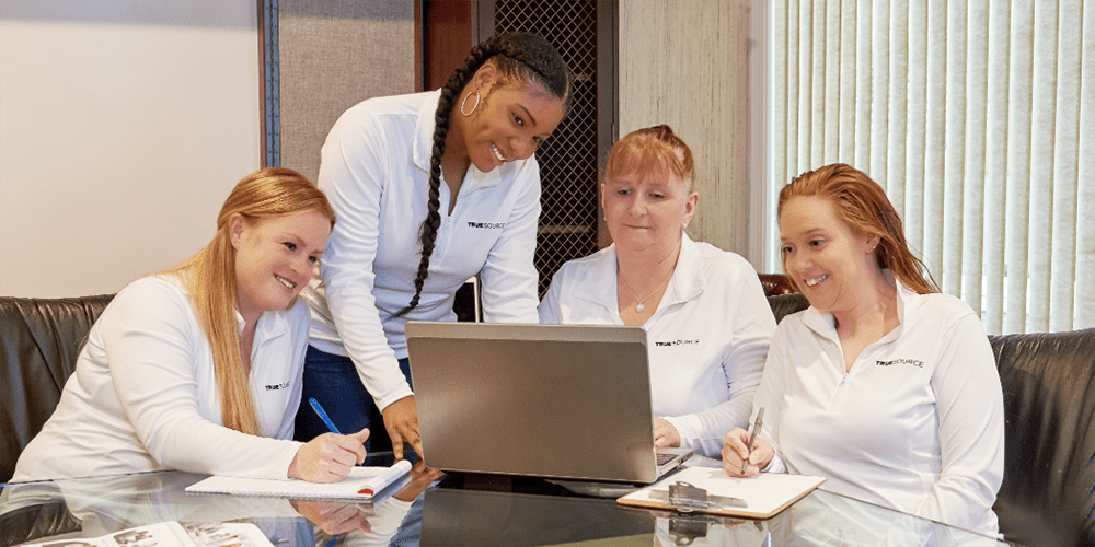 truesource employees working together at a computer and smiling